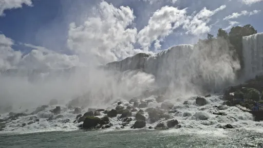 Waterfall cascading over rocks with mist and a cloudy sky.