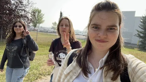 Three people walking outside on a sunny day, two showing peace signs.