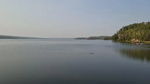 Calm lake with a forested shoreline under a clear blue sky.