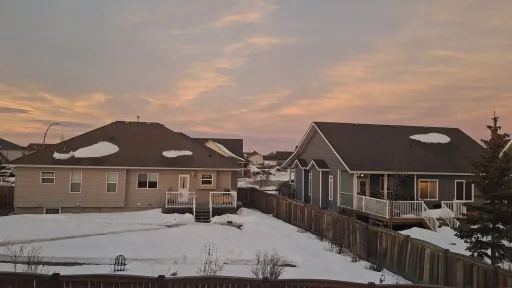 Suburban houses with snow-covered yards at sunset.
