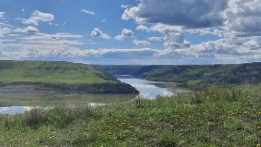 Grassy hillside overlooking a river under a cloudy blue sky.