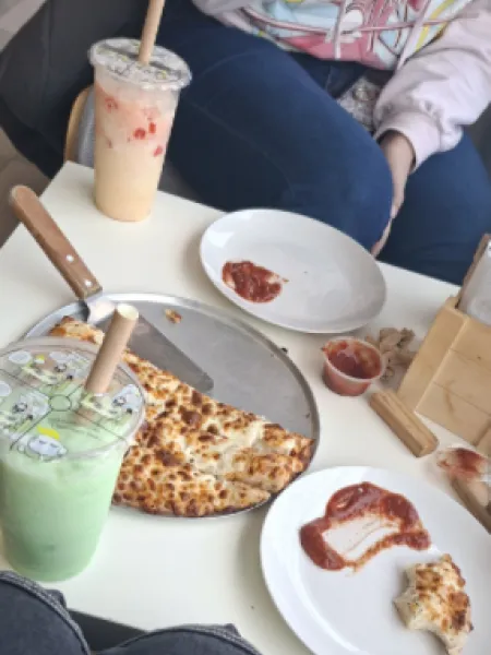 Pizza and bubble tea on a table, with people seated nearby.