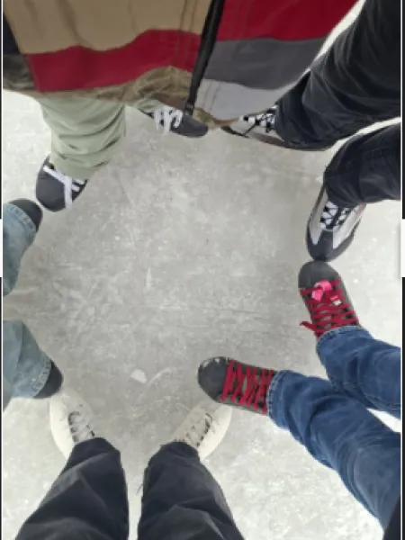 Top-view of five people from the waist down with ice skates standing in a circle