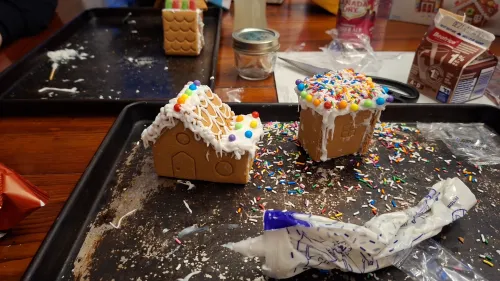 Gingerbread houses with icing and colorful sprinkles on a tray.