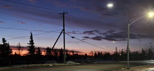 Street at dusk with power lines and glowing streetlights.