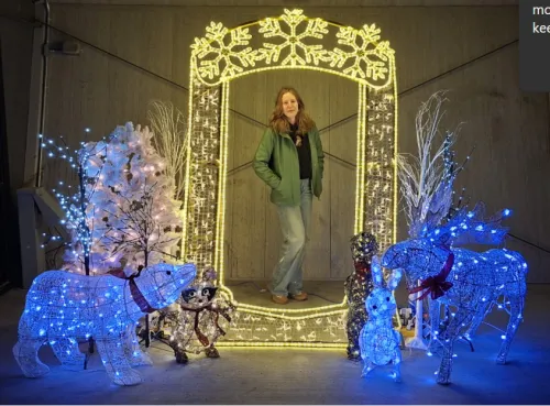 Woman standing in illuminated arch, surrounded by festive lights and decorations.