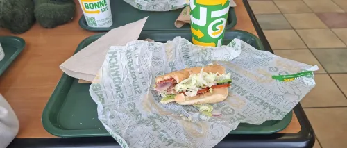 Half-eaten sandwich from subway and drink cup on a tray in a casual dining setting.