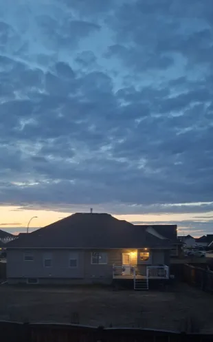 House at dusk with a cloudy sky, one window warmly lit.
