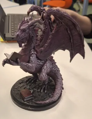 Shimering purple dragon figurine holding book.