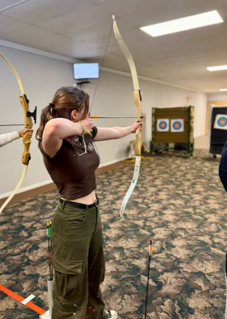 Archer aiming at a target indoors, wearing casual clothes.